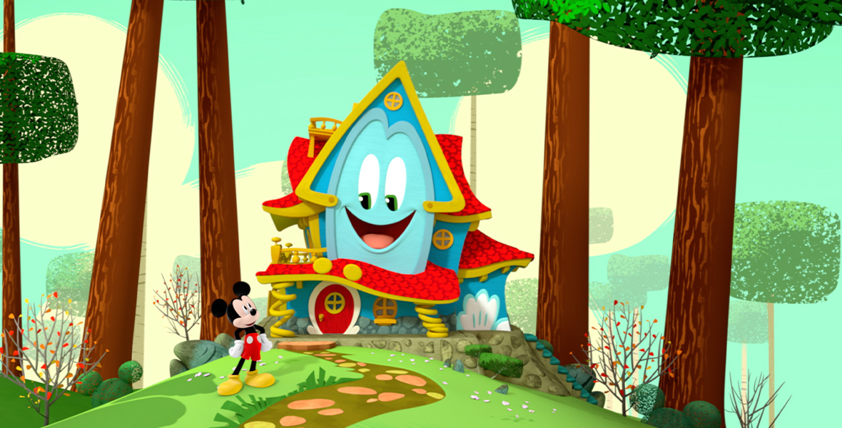 In a promotional image for Mickey Mouse Funhouse, the enchanted talking playhouse Funny (voiced by Harvey Guillén) is seen in a forest setting, and Mickey Mouse (voiced by Bret Iwan) is standing to their left, looking up at them. Trees surround Funny on either side, and there is a path leading up to Funny’s front door.