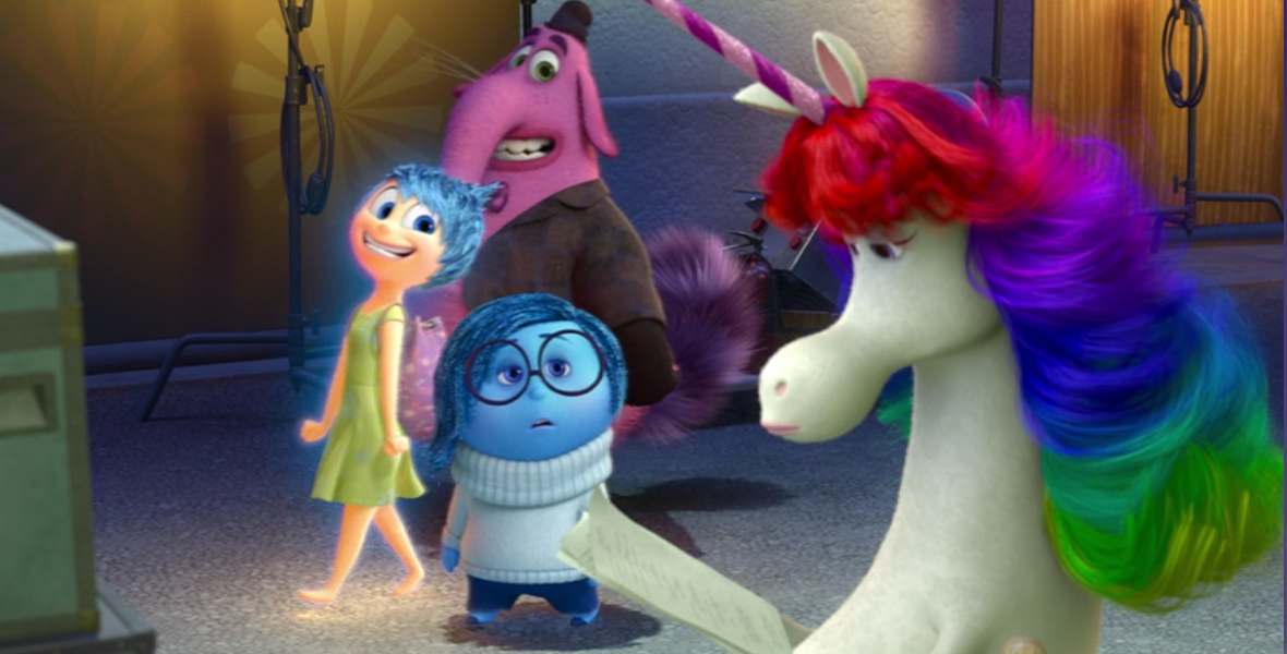 In a scene from Inside Out, Rainbow Unicorn, a white unicorn with a rainbow mane, reads a script in the foreground. Behind her, Sadness, Joy, and Bing Bong walk past. Joy and Bing Bong can barely contain their excitement, while Sadness looks at Rainbow Unicorn without much interest.