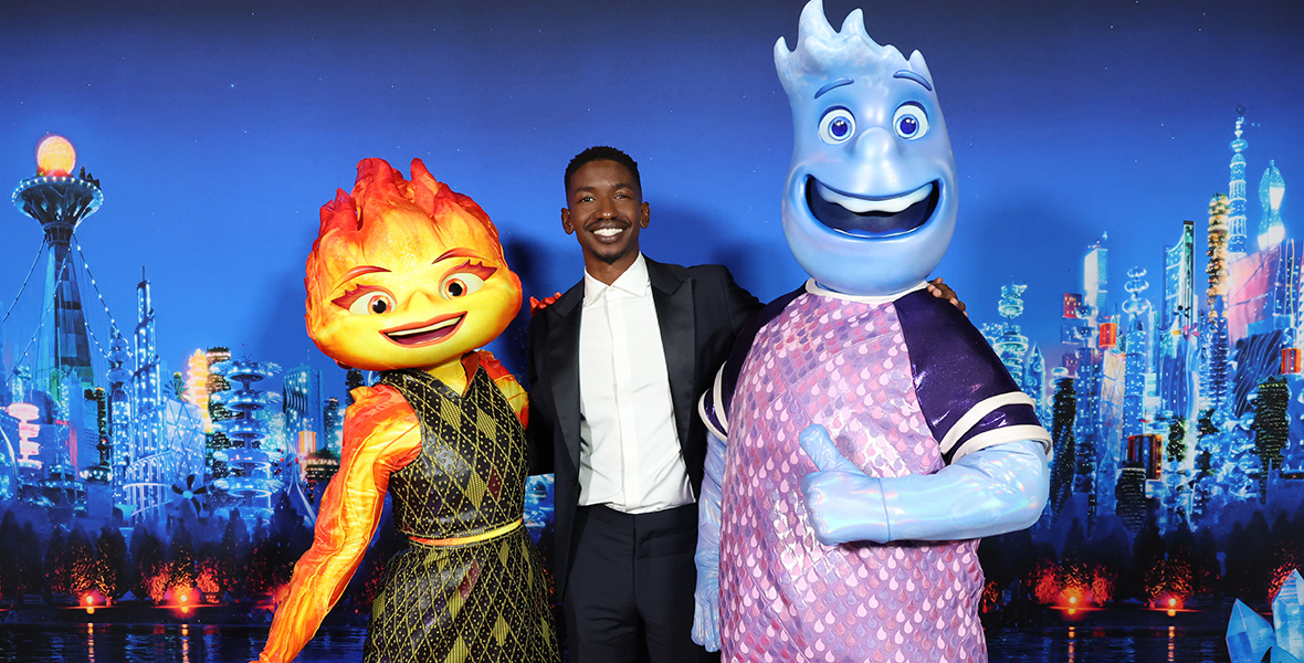 Mamoudou Athie poses in front of an Element City-based backdrop with the character he voices, water-based Wade, along with Ember.
