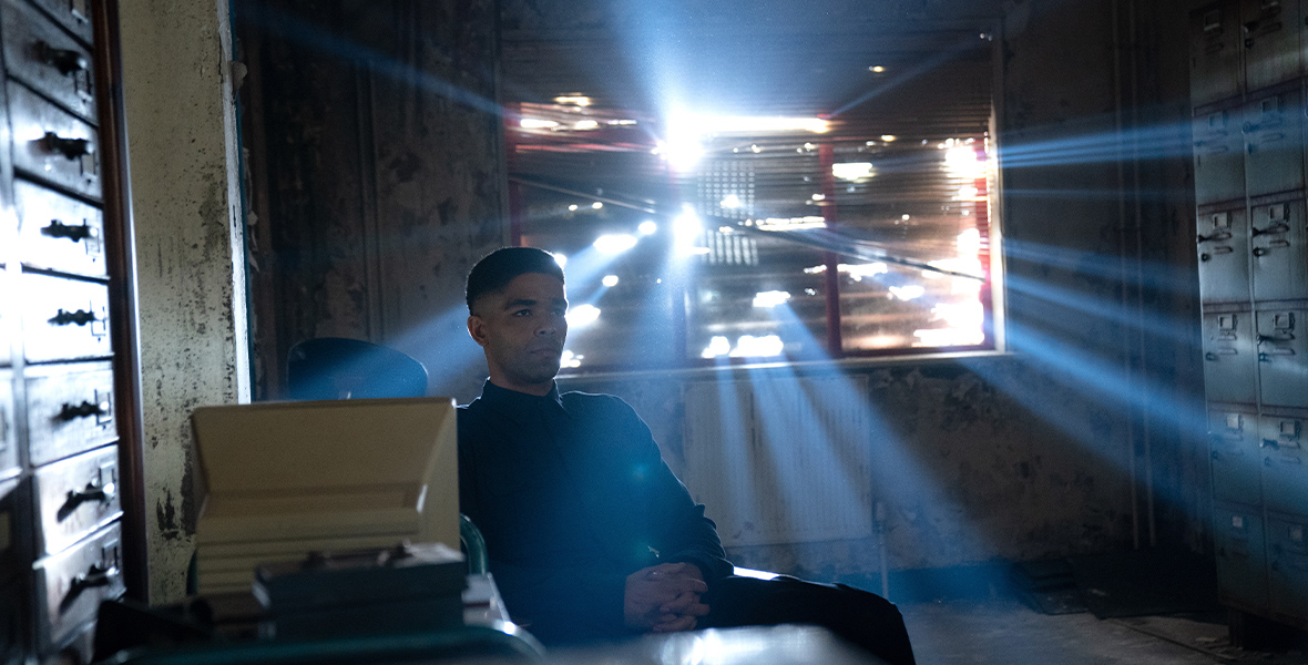 The rebel Skrull leader Gravik (Kingsley Ben-Adir) sits alone, with his hands clasped, in an abandoned room. Sunlight pours in from the broken window behind him.