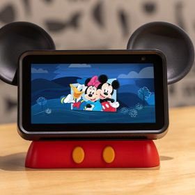 The Hey Disney device sits on a coffee table. The device is a tablet with mouse ears, stylized to look like Mickey Mouse, featuring an image of Donald, Minnie, and Mickey on the screen.