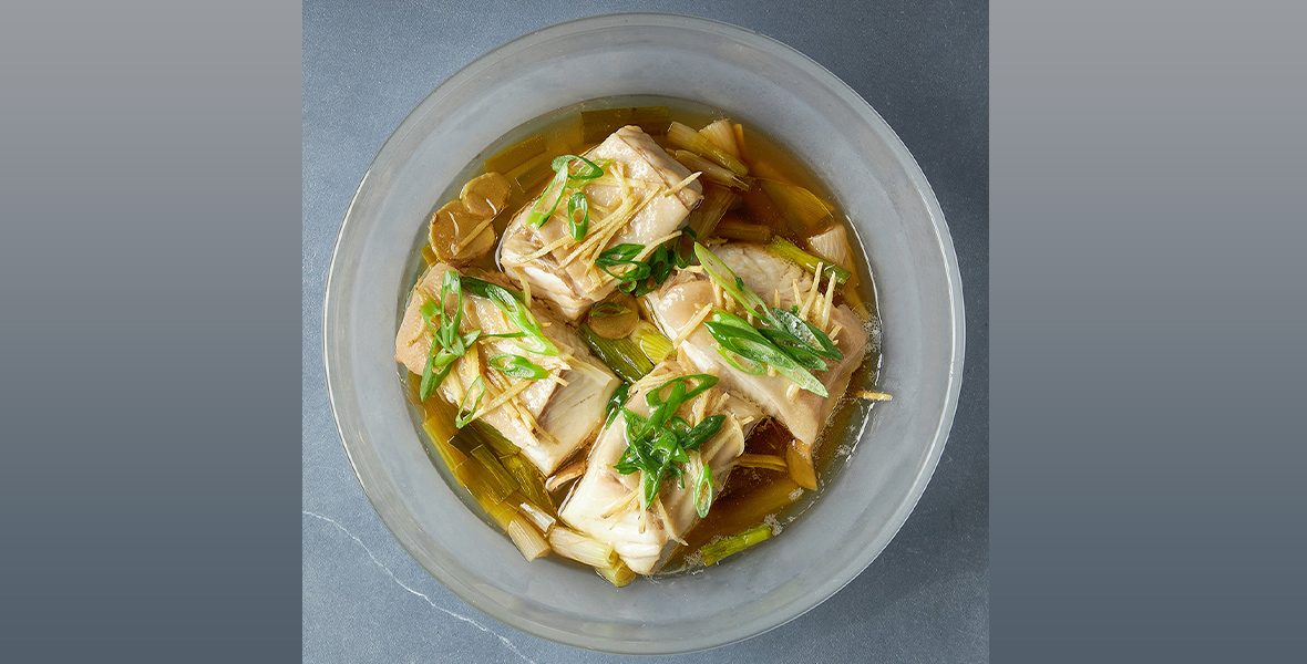Steamed fish in a gray bowl, photographed from above. The fish is topped with scallion and ginger.