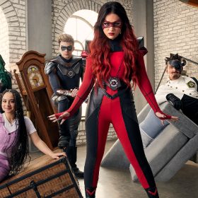 Amy, Colby, Jake, Eva, and Vic are in their supervillain outfits standing around furniture while Hartley is in lilac overalls.
