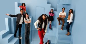 A promotional image from Disney Channel’s Pretty Freekin Scary, featuring Kyan Samuels as Pretty, Yonas Kibreab as Remy, Leah Mei Gold as Scary, Eliana Su’a as Frankie, Emma Shannon as Nyx, Shawn Carter Peterson as Mr. Ripp, and Napiera Groves Boykin as Mrs. Ripp. They are all standing on a light blue set that features a series of strange stairways going in different directions, and appears as though the floor they’re standing on is a funhouse-type mirror. The actors are all smiling at the camera.