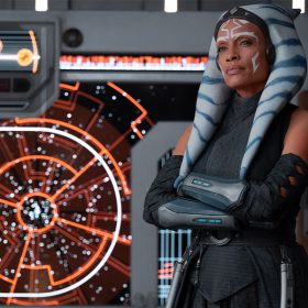 Jedi Knight Ahsoka Tano (Rosario Dawson) stands with her arms crossed in a space craft setting. Controls glowing behind her