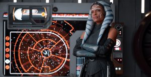 Jedi Knight Ahsoka Tano (Rosario Dawson) stands with her arms crossed in a space craft setting. Controls glowing behind her