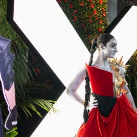 A guest posed in front of an illuminated X-Men logo on the green carpet at D23’s X-Men Hellfire Gala Event. They’re wearing an outfit inspired by Marvel Comics character Rasputin IV.