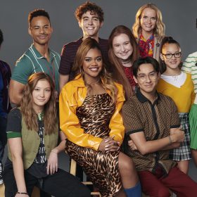 A cast photo from Season 4 of High School Musical: The Musical: The Series features, from left to right, Monique Coleman, HIGH SCHOOL MUSICAL: THE MUSICAL: THE SERIES – Disney’s “High School Musical: The Musical: The Series” stars Larry Saperstein as Big Red, Adrian Lyles as Jet, Mark St. Cyr as Mr. Mazzara, Saylor Bell as Maddox, Dara Reneé as Kourtney, Joshua Bassett as Ricky, Julia Lester as Ashlyn, Frankie A. Rodriguez as Carlos, Kate Reinders as Miss Jenn, Liamani Segura as Emmy, Sofia Wylie as Gina, and Matt Cornett as EJ. Cast members are all in colorful clothing and are standing or seated in front of a neutral gray background.