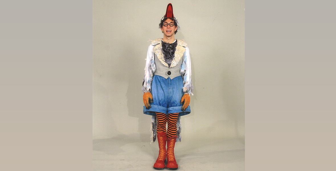 Tim Federle, series creator and executive producer for High School Musical: The Musical: The Series, stands in front of a neutral gray backdrop in his seagull costume for the Broadway production of The Little Mermaid from some years ago. The costume includes baggy blue shorts over striped leotards and red boots, as well as white bird-feather sleeves, a gray vest, and a beak-shaped hat. He’s also wearing round eyeglasses and bird-claw gloves.
