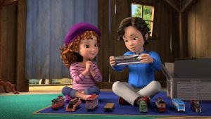 Nancy sits with hands-clasped on a blue carpet as Sean, her cousin Lionel’s favorite cousin, sits next to her as he shows her the front car of his model train set. An open box is to his right and the rest of the train sits in perfect neat vertical rows in front of them.
