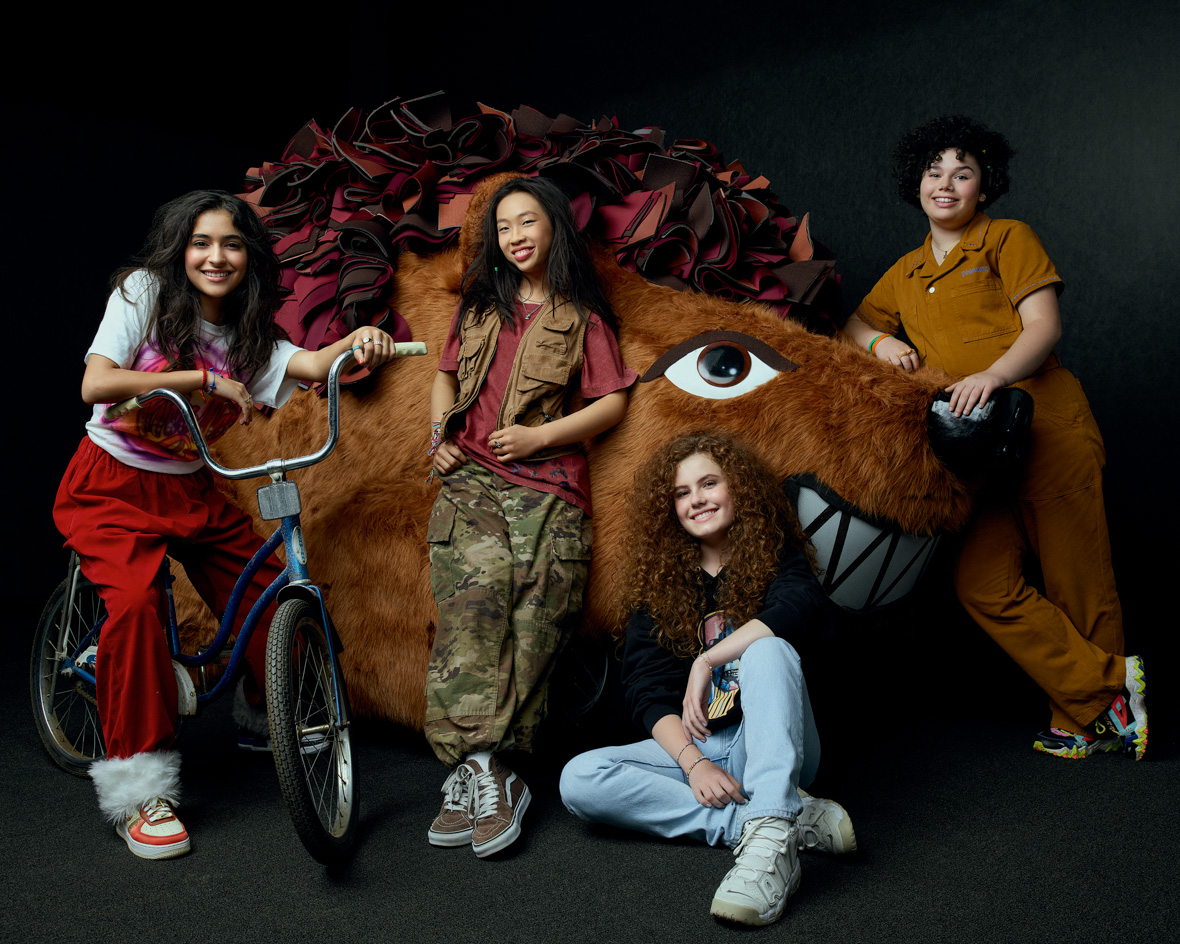 In a promo image for the Disney Channel Original Movie The Slumber Party, from left to right, are Valentina Herrera as Anna Maria, Emmy Liu-Wang as Paige, Darby Camp as Megan, and Alex Cooper Cohen as Veronica. They’re flanking a huge stuffed hedgehog of some kind; additionally, Herrera is sitting on a bicycle. She is wearing a graphic tee and red pants; Wang is wearing a dark red shirt, a brown vest, and camo pants; Camp is wearing a black graphic tee and jeans; and Cohen is wearing a dark mustard yellow jumpsuit.