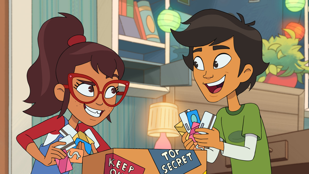 In an image from Disney Branded Television’s Hailey’s On It!, Hailey (voiced by Auli’i Cravalho) and Scott (voiced by Manny Jacinto) are grabbing handfuls of credit cards from inside a cardboard box labeled “Top Secret” and “Keep Out.” Hailey is wearing blue jean overalls, a red and white long-sleeved T-shirt, and red glasses; Scott is wearing a green T-shirt over a white long-sleeved shirt.