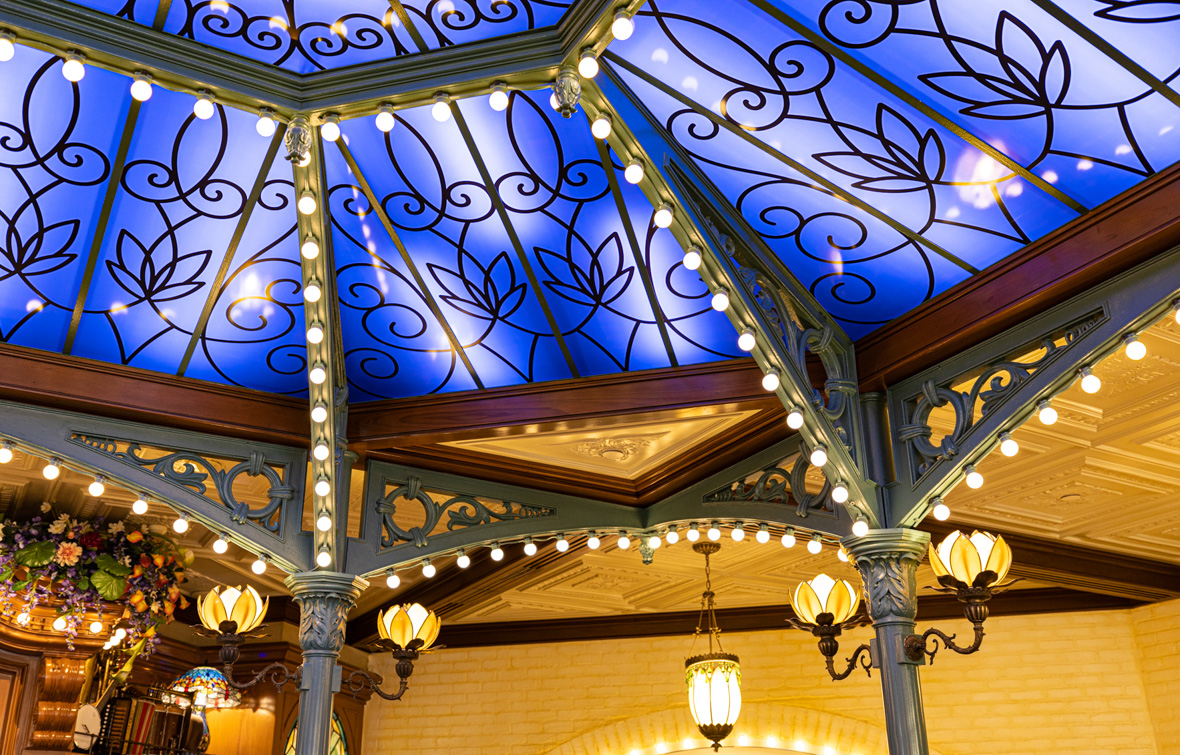 The skylight at Tiana’s Palace is made up of blue glass and held up by wooden beams lined with white lightbulbs.