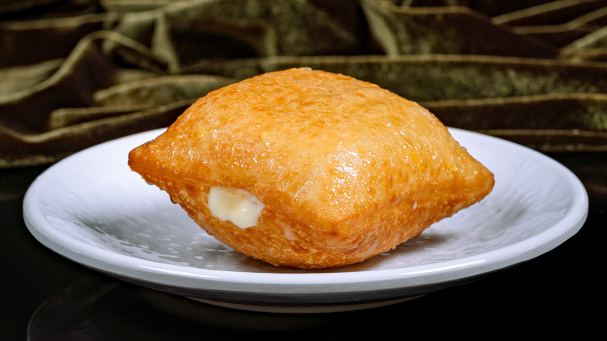 A golden brown beignet with lemon pie filling sits on plate at Tiana’s Palace. This is the lemon-glazed House-Filled Beignet.