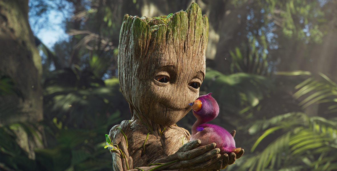 Baby Groot from I Am Groot, holds a purple bird in his hands and looks at it lovingly while standing in a forest, surrounded by greenery.