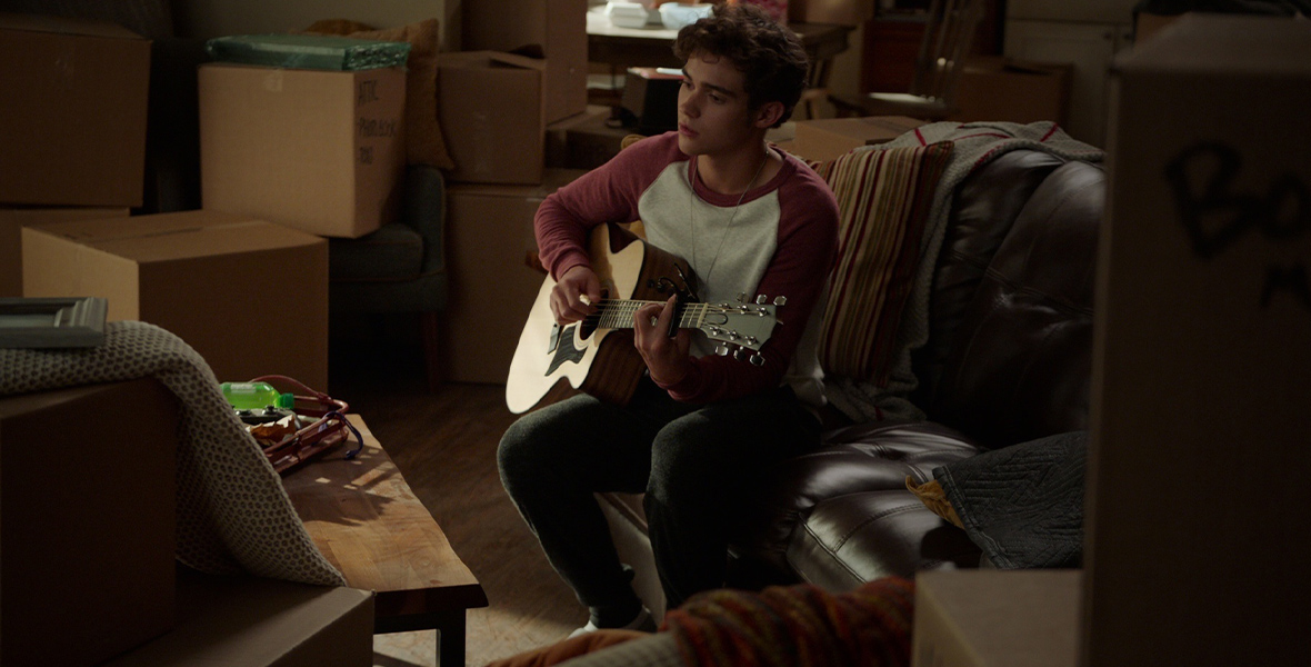 In a scene from the High School Musical: The Musical: The Series episode “Valentine’s Day,” Ricky Bowen, played by Joshua Bassett, plays guitar amid a sea of boxes.