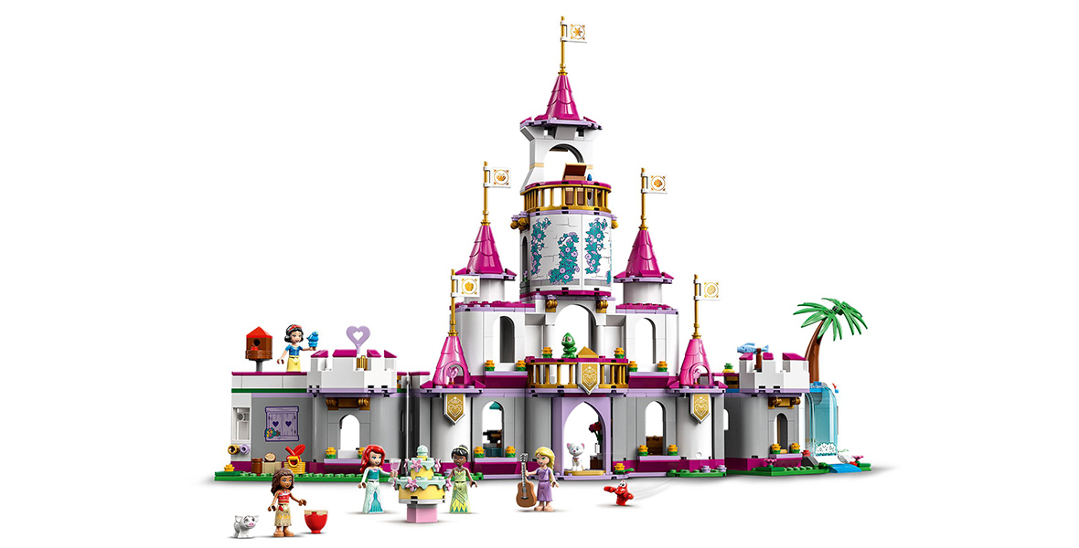 A LEGO castle set, featuring mini figures of Moana, Snow White, Ariel, Tiana, and Rapunzel. All princesses except for Snow White are gathered by a cake in front of the castle. Snow White is standing on a castle balcony, next to a bird house, with a bluebird perched on her hand.