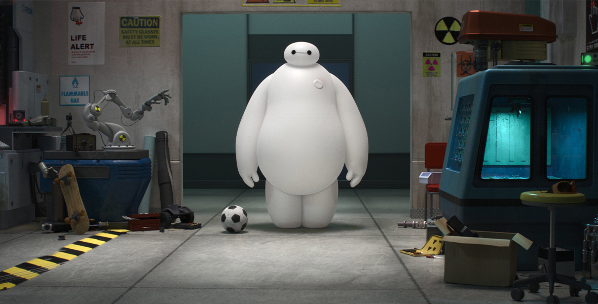 Baymax, from Big Hero 6, stands in a concrete room with several objects around him including a soccer ball, robotic hand, blue machine, caution sign, cardboard box, and several other unidentified tools.