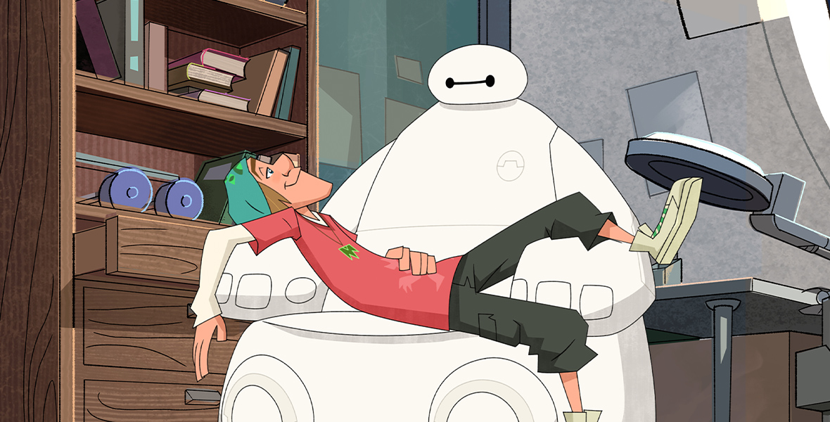 Fred, from Big Hero 6, is wearing a white long sleeve shirt under a red short sleeve shirt, green cargo shorts, white high-top sneakers, and a green hat while he sits in Baymax’s lap. To the left of them is a bookshelf with books on the top shelf, blue arm weights on the bottom shelf, and three drawers under the shelves with the top drawer pulled out. To the right of them is a gray light.