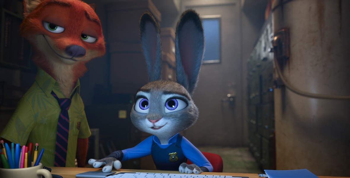 In a still from Walt Disney Animation Studios’ Zootopia, from left to right, Nick Wilde (voiced by Jason Bateman) and Judy Hopps (voiced by Ginnifer Goodwin) are in a darkened room; Nick is standing next to Judy, who’s sitting at a desk looking at a computer that’s just off screen. They both look intrigued regarding whatever contents the computer screen is showing them.
