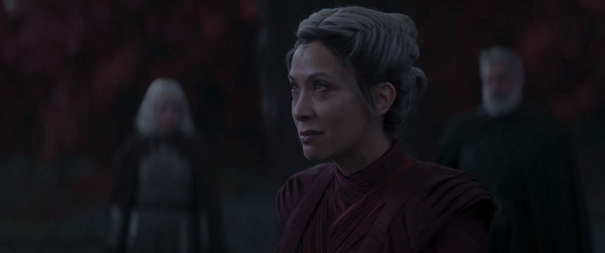Morgan Elsbeth (Diana Lee Inosanto) sneers at something off camera, her white hair pulled back with braids. Out of focus in the darkness behind her are Shin Hati (Ivanna Sakhno) and Baylan Skoll (Ray Stevenson).