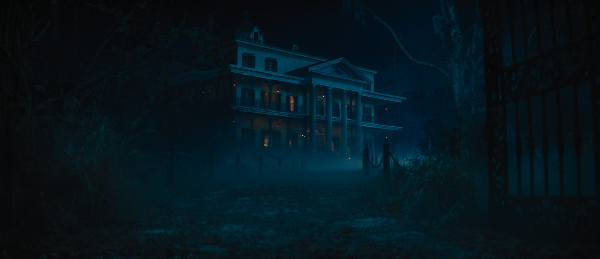 A still from the 2023 film Haunted Mansion, showing the exterior of the mansion at nighttime. In front of the mansion, a fence leads towards the camera.