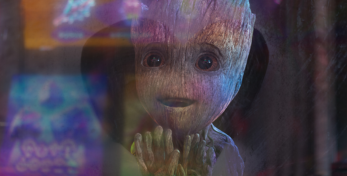 Baby Groot, from I Am Groot, is seen through a foggy window that has a heart shape wiped out of it to reveal his face. Groot looks in awe at something out the window that creates a colorful reflection of blues, pinks, and purples.