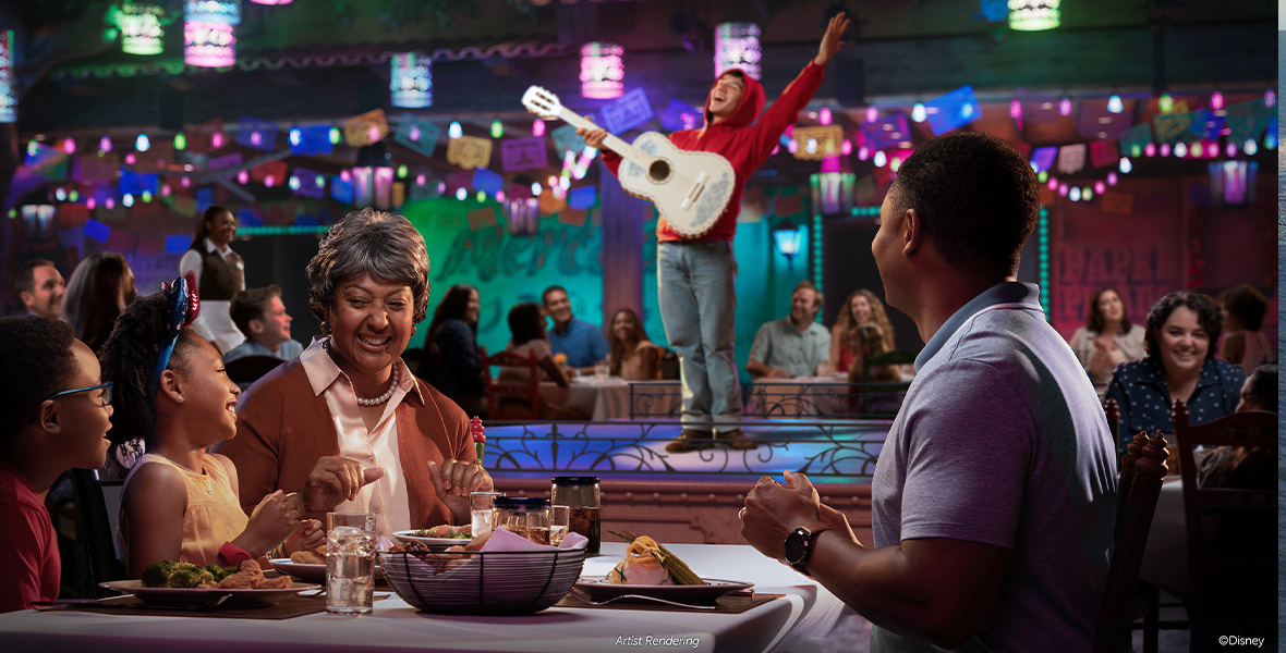 In an artist’s rendering of Plaza de Coco onboard Disney Cruise Line’s Disney Treasure, a family of four—a grandmother, a father, and two young children—sits at a table and enjoys a meal while a performer dressed as Miguel from Disney and Pixar’s Coco is on stage, playing a white guitar and singing. The room is full of colorful lanterns and flags, and other families and waitstaff are watching the performer as well. The performer is dressed in a red hoodie and jeans.