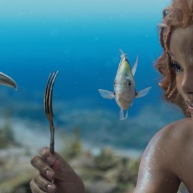 In a scene from The Little Mermaid, Ariel, played by Halle Bailey, holds out a fork and smiles at Scuttle, voiced by Awkwafina, as Flounder, voiced by Jacob Tremblay, swims beside Ariel.
