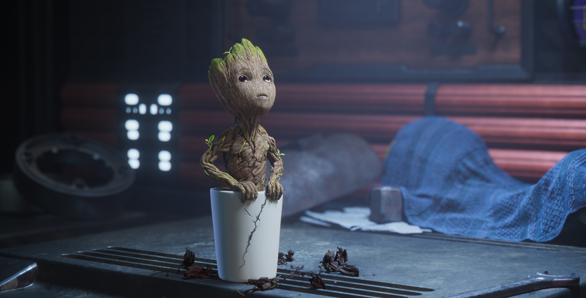 In an image from the second season of Disney+’s I Am Groot, Baby Groot (voiced by Vin Diesel) is sitting in his small white flowerpot, which has a crack in its side, and is looking up at something off camera. There are some bits of dirt surrounding the pot, and the pot itself is sitting on a table—seemingly inside one of the Guardians’ spaceships.