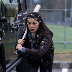 In the Goosebumps episode "Cuckoo Clock of Doom," actor Ana Yi Puig holds a baseball bat and crouches between two cars. Puig and the cars are covered in green goo.