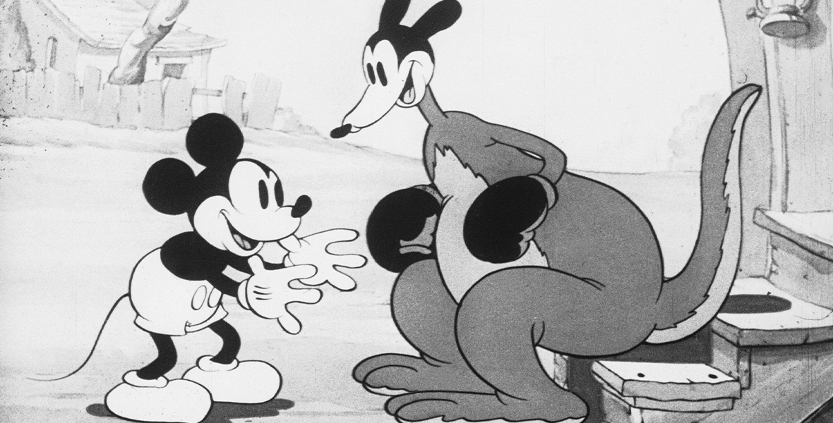 Mickey Mouse stands with both arms outstretched. Mickey faces a smiling kangaroo, who is wearing boxing gloves and is standing at the bottom of a short staircase.