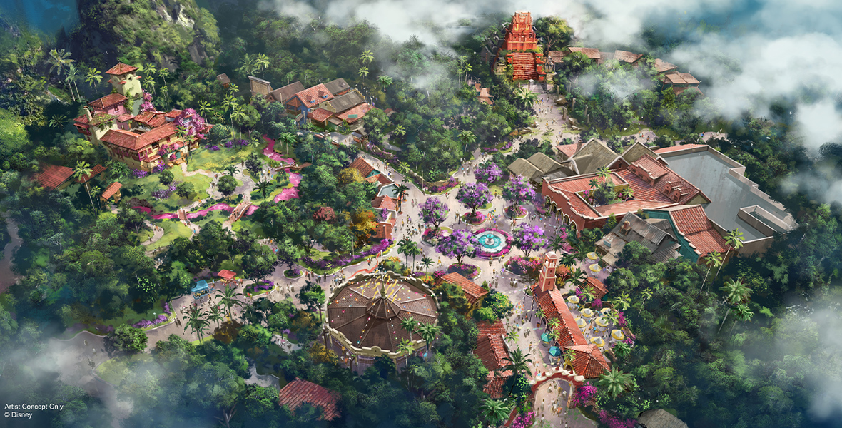 An aerial view concept painting of the possible new land in Disney’s Animal Kingdom features a rounded building with lights on the roof, red roofed buildings, a fountain surrounded by pink flowers, lots of foliage including palm trees that line the beige pathways, and an arched entrance.