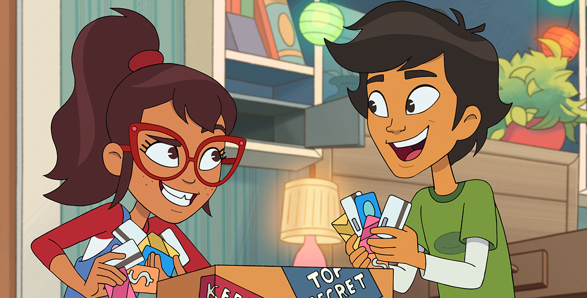 In an image from Disney Branded Television’s Hailey’s On It!, Hailey (voiced by Auli’i Cravalho) and Scott (voiced by Manny Jacinto) are grabbing handfuls of credit cards from inside a cardboard box labeled “Top Secret” and “Keep Out.” Hailey is wearing blue jean overalls, a red and white long-sleeved T-shirt, and red glasses; Scott is wearing a green T-shirt over a white long-sleeved shirt.