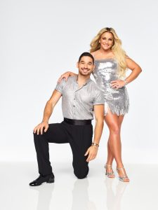 Jaimie Lynn Spears has on a reflective silver dress with one hand on her hip and the other around Alan Bersten’s neck. He has one knee on the floor and the other bent.