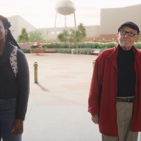 In a scene from the short film Once Upon a Studio, an intern and Disney Legend Burny Mattinson stand just outside of the doors of the Roy E. Disney Animation Building in Burbank, California. The Walt Disney Studios Water Tower is just visible in the background.
