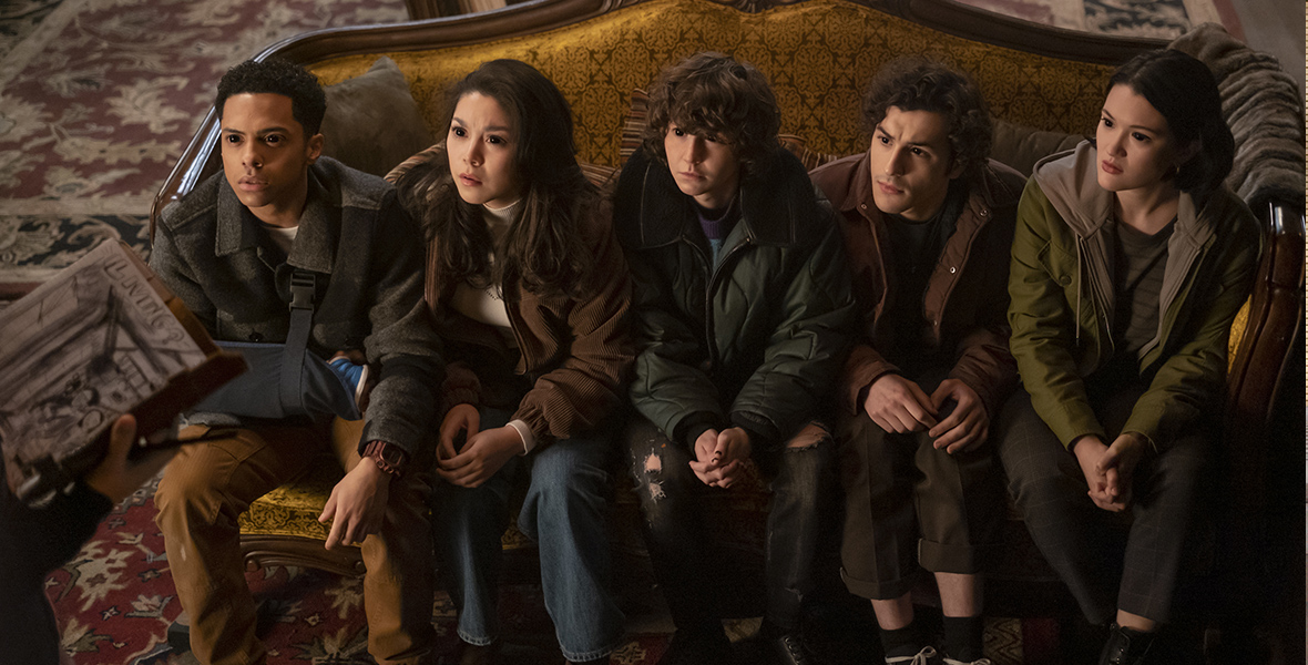 In an image from the Disney+ and Hulu series Goosebumps, cast members (from left to right) Zack Morris, Ana Yi Puig, Miles Mckenna, Will Price, and Isa Briones are sitting on a couch and looking up at someone off camera to the left. All of their eyes are black.