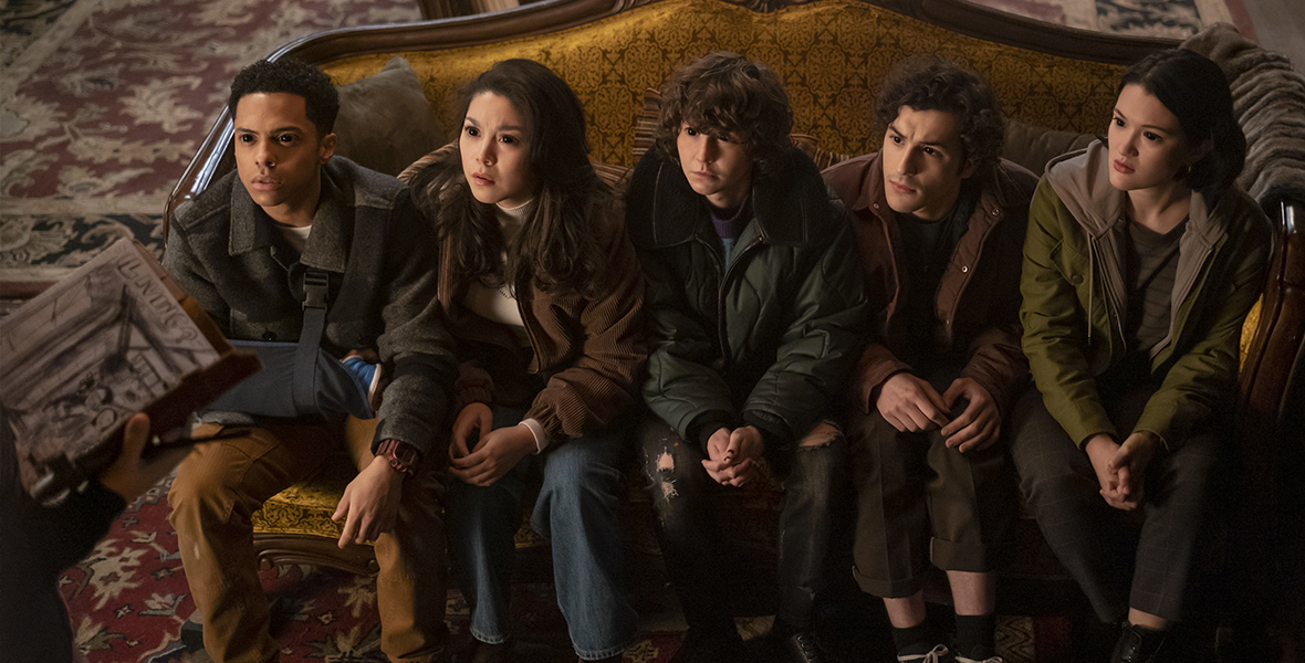 In an image from the Disney+ and Hulu series Goosebumps, cast members (from left to right) Zack Morris, Ana Yi Puig, Miles Mckenna, Will Price, Isa Briones are sitting on a couch and looking up at someone off camera to the left. All of their eyes are black.