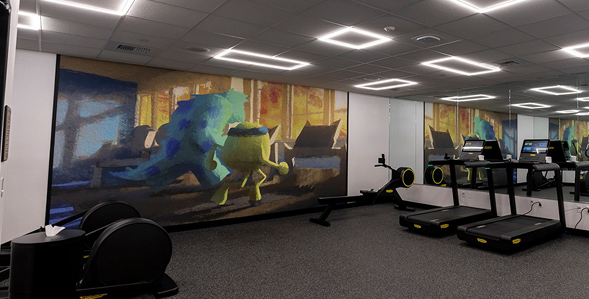 The fitness room features aerobic equipment and a large mural filling one wall with an image of Sully and Mike from Monsters Inc. working out on treadmills.