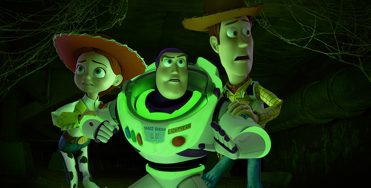In an image from Disney and Pixar’s Toy Story of TERROR!, from left to right, Jessie (voiced by Joan Cusack), Buzz Lightyear (voiced by Disney Legend Tim Allen), and Sheriff Woody (voiced by Tom Hanks) are huddled together and appear a bit frightened. They are bathed in mysterious green light.