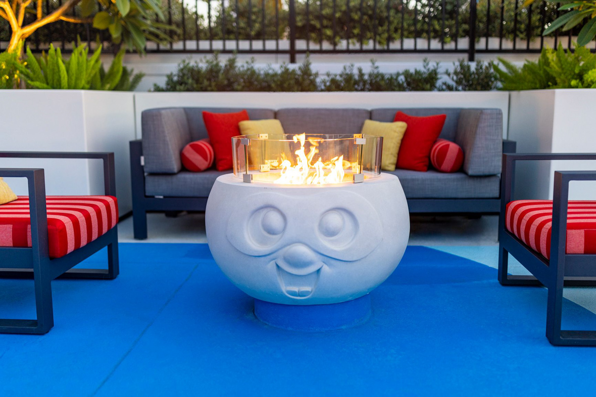 The pool-side fireplaces are large blocks of concrete with faces on them, so the fire burning at the top appears to be flaming hair.
