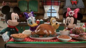 Standing around a table set with a holiday meal in a log cabin are four stop-motion Disney characters, all, except Pluto, dressed in Christmas attire. Pictured from left to right are Mickey Mouse, Daisy Duck, Pluto, and Minnie Mouse. In front of them, on the table, are two pies; a roasted turkey on a platter; baked beans in a bowl; and two more serving dishes holding various treats. Behind them is a galley kitchen with a few Christmas decorations. Visible are a refrigerator, cabinets, a counter holding red and green mugs, a sink, a stovetop venting hood, and a window with white curtains. Outside the window, it’s snowing.