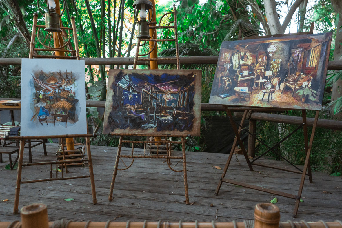 Three paintings are lined up, each sitting on an easel, on a terrace or platform. From left to right, the paintings portray the twin boys’ nature-themed room, the daughter’s astronomy-themed room, and the mother’s music room.