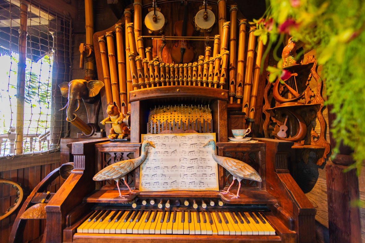 An elaborately carved and constructed pipe organ is automated to play on its own. Above the keyboard is the turning cylinder that determines the music to be played, and above that are pipes that appear to be made from bamboo. Behind and above the pipes are a self-playing violin and two tambourines. Various animal figurines stand in different positions around the instrument, including an elephant, a squirrel, and two cranes.