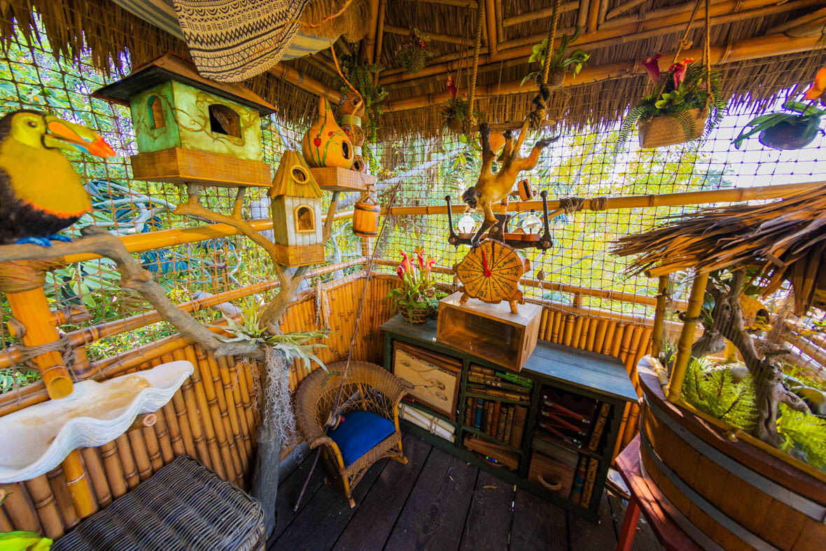 The twin boys’ room features their pet monkey, Rascal, hanging from the ceiling at the center; a toucan perched on the left; a series of birdhouses beyond the toucan along the left wall; and a frog incubator, partially visible on the right. Plants in pots also hang from the ceiling.