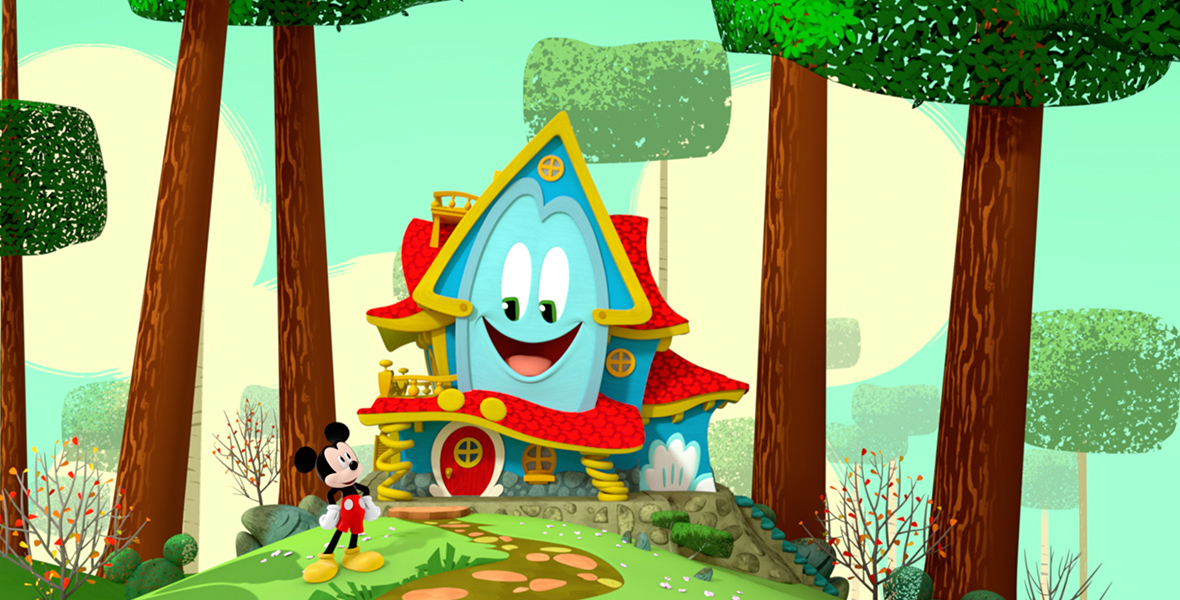 In an image from Disney Branded Television’s Mickey Mouse Funhouse, Funny the funhouse (voiced by Harvey Guillén) is seen at the end of a stone path, surrounded by trees. He has a red thatched roof and door and big expressive eyes. To his left, standing near the stone path, is Mickey Mouse (voiced by Brett Iwan).