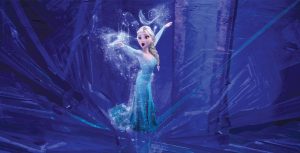 Elsa stands with her arms outstretched, sparkly magic surrounding her as she sings inside her ice palace.