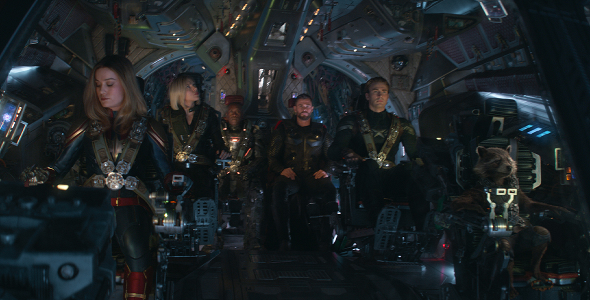 A screenshot from Avengers: Endgame, features characters sitting in a spaceship. The characters include (from left to right) Captain Marvel, played by Brie Larson, Black Widow, played by Scarlett Johansson, James Rhodes, played by Don Cheadle, Thor, played by Chris Hemsworth, and Captain America, played by Chris Evans.