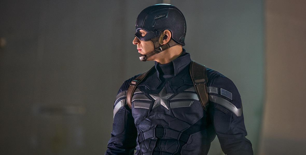 Steve Rogers aka Captain America, played by Chris Evans, in Captain America: The Winter Soldier is wearing a blue suit with a silver star on the front of and a blue helmet on his head. His head is turned to the right and he has a serious look on his face.