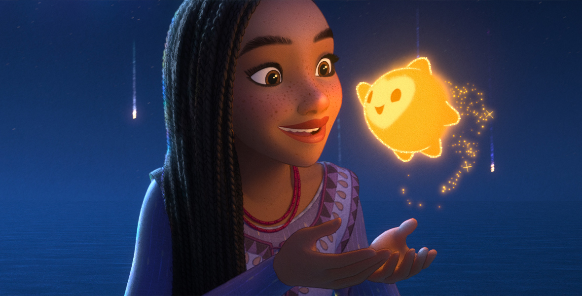 In a scene from Walt Disney Animation Studios' Wish, Asha's face is illuminated by Star—a little ball of boundless energy. Asha is smiling and cups her hands underneath Star.